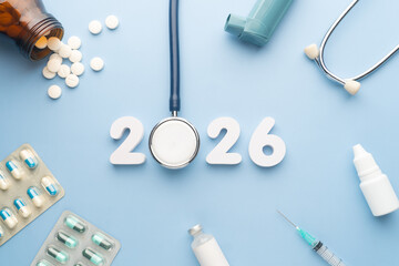 2026 Happy New Year banner for health care and medical concept. Stethoscope with doctor pills, syringe, vaccine vial, eyes drop, antibiotics and white number 2026 on table blue background.