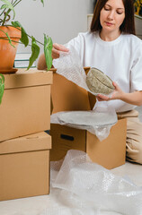 Portrait of woman wearing white t-shirt sitting on the floor surrounded with carton boxes and packing plates and dishes. Relocating, buying new house. Pack personal stuff from carton boxes. 