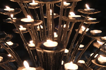 Close up of a wrought iron candelabra filled with lit votive candles inside a church