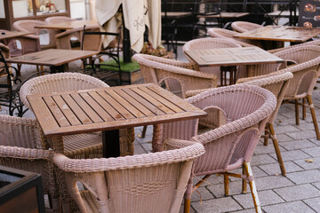 Cafe chairs and tables on outdoor wicker terrace patio, empty arrangement of wooden furniture at sidewalk bistro, cozy dining scene for morning relaxation and urban hospitality.