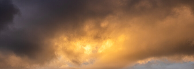Panoramic image of powerful storm clouds illuminated by bright golden and orange light of the evening sunset Dramatic richly textured sky creating an atmospheric background for copy space