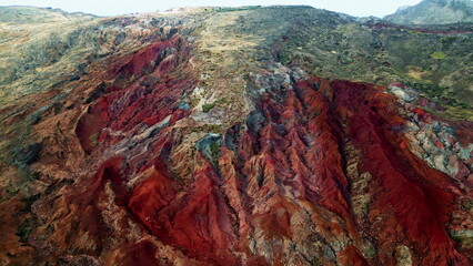 Aerial eroded red cliffs with layered rock textures stones sparse vegetation.