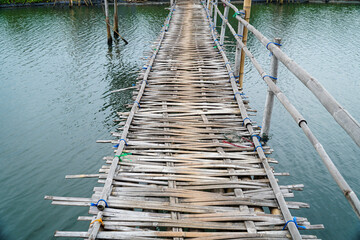 Fototapeta premium Rustic charm is captured in this old, weathered bamboo bridge stretching across tranquil waters. The detailed textures and simple construction evoke a sense of serenity and rural escape.