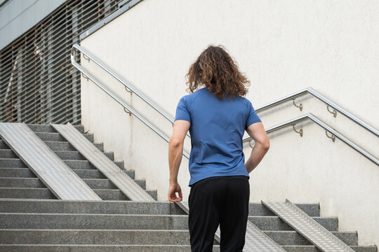 Sporty man and athlete wearing blue t-shirt running at stair in modern city. Cardio workout training. Back view. Healthy lifestyle. Wellness - Powered by Adobe