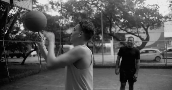 Two men passing spinning basketball on court, teamwork and friendship expressed through pensive concentration in black and white outdoor sports practice with balance and coordination - Powered by Adobe