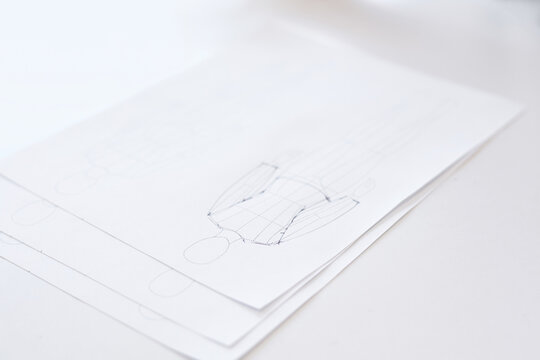 Sheets of paper with sketches of garment lying on white table in atelier, close-up view