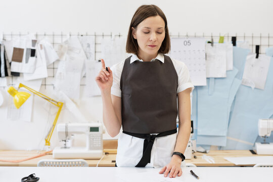 Creative custom tailor at work. Caucasian woman working on new collection of garment, standing by table and drawing sketches on paper