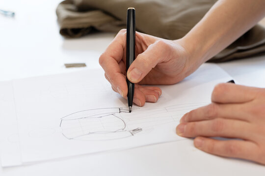 Close-up view of unrecognizable female designer drawing sketch of garment on sheet of paper with felt-tip pen