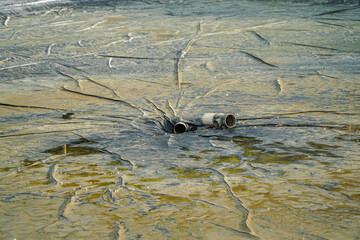 A textured outdoor surface with water and scattered drainage pipes conveys an abstract industrial landscape. Captured in bright daylight, its unique and rugged aesthetic can offer visual intrigue.