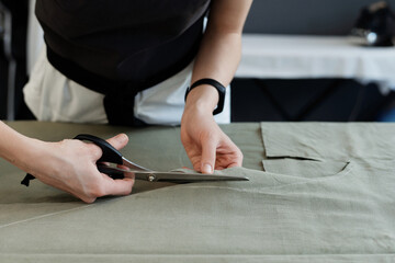 Close-up view of unrecognizable female seamstress cutting tracings out of fabric for sewing new garment