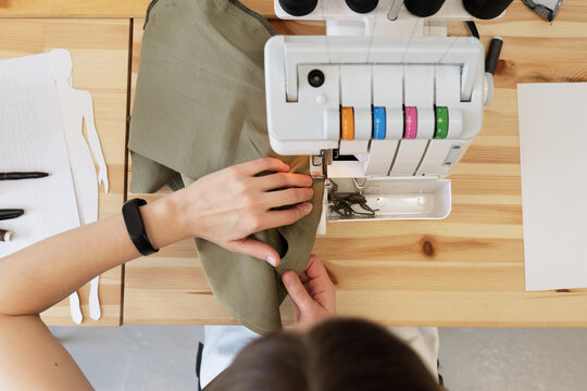 Directly above view of unrecognizable dressmaker sitting at table and sewing garment on modern sewing machine