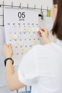 Rear view of unrecognizable woman unsticking notes with accomplished plans from calendar hanging on wall