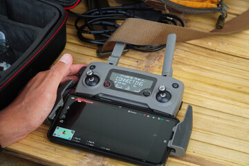Preparing for aerial adventures with modern technology. The drone controller connects to a smartphone, offering control and a real-time view for capturing breathtaking aerial footage and images. © Pernandi Imanuddin