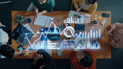 A team of professionals collaborates over a table filled with documents and technology, exploring financial data visualization through digital charts and graphs. Scalp