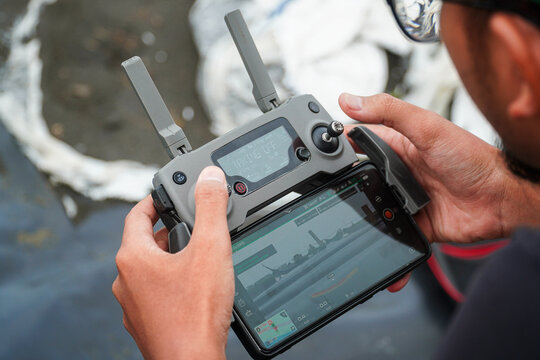 Close-up shot captures a person operating a drone remote with a smartphone attached, seemingly for observation or control, suitable for showcasing modern farming technology and innovation.