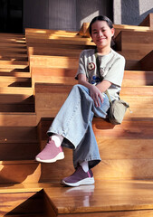 Happy Asian Preteen Girl Sitting on Indoor Wooden Stairs