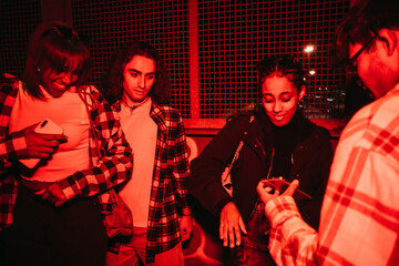 Side view of group of diverse friends listening to music from mobile phone and dancing at night with a red light