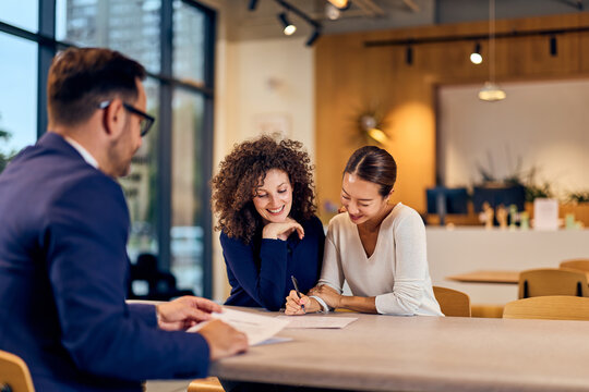 Collaborative Meeting At Modern Office Café With Two Women And A Man Reviewing Documents