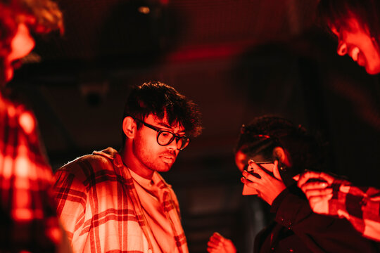 Side view of group of diverse friends listening to music from mobile phone and dancing at night with a red light