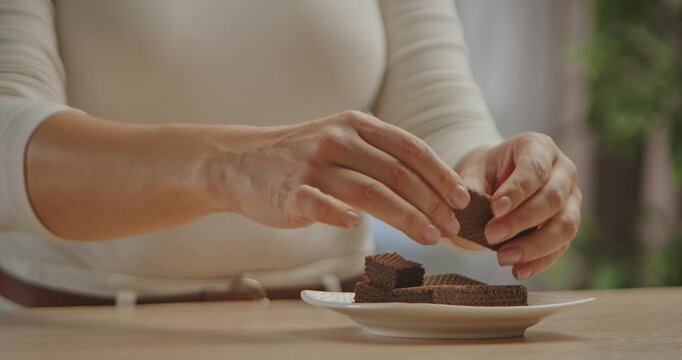 Close up of hands breaking crispy chocolate wafers onto a white plate, demonstrating how to make a homemade dessert. Slow motion.
