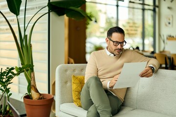Professional Man Reading Document in Modern Office Lounge Setting With Plants