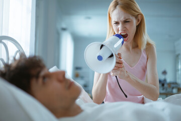 A white woman screams into a megaphone at her sleeping husband, trying to wake him up in the...