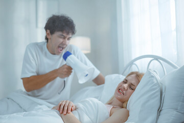 Obraz premium A white man shouts into a megaphone at his sleeping wife, trying to wake him up in the morning.