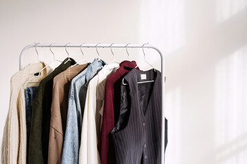 A fall capsule wardrobe on a white rail hanger in a sunny white room. Copy Space.