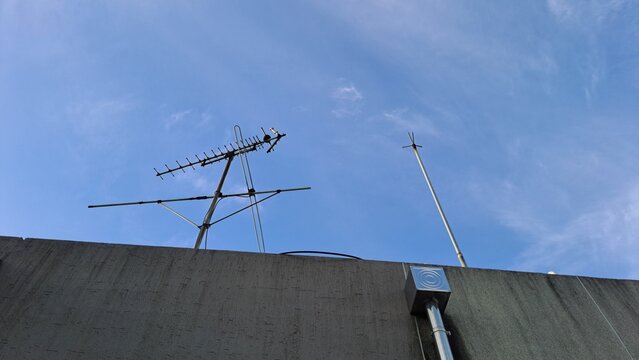 old tv antenna and lightning rod on a rooftop against a clear blue sky