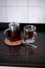 brewing tea in a glass teapot and next to it is a glass mug with herbs and crumbly tea scattered on...