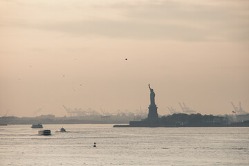 Estatua de la Libertad al atardecer en la Isla Ellis. Vista de la Bah&iacute;a Superior en el horizonte con la Estatua de la Libertad y la ciudad de Nueva Jersey al fondo a la puesta del sol. NYC.