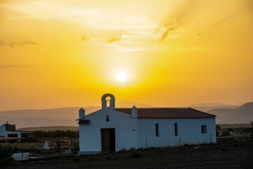 White rural chapel at sunset with a bell silhouette and bright sky, in Aljibe Quebrao - Guadix