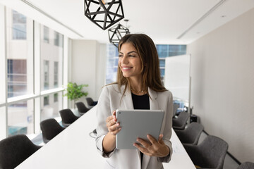 Happy dreamy young Hispanic business professional woman holding tablet