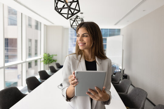 Happy dreamy young Hispanic business professional woman holding tablet