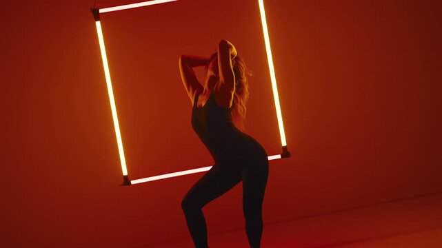 Camera rotates around its own center slowly pulling away from the woman as she dances against glowing neon square