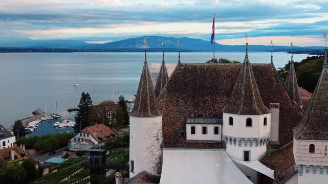 Aerial view of the magnificent Nyon Castle, its flag fluttering proudly amidst the backdrop of the serene lake, Nyon, Vaud, Switzerland.