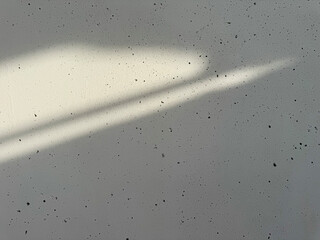An abstract close-up of a speckled, gray concrete wall texture with a diagonal band of bright sunlight and shadow cast across the surface.
