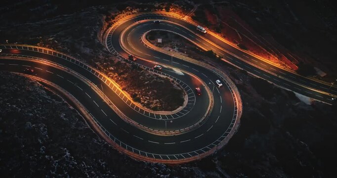 Malta: Night traffic. Cars driving on a winding road at sunset illuminating the Maltese landscape with orange street lights, creating a mesmerizing aerial view. Static shot
