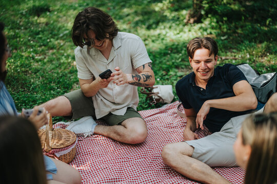 A group of friends gathered on a picnic blanket, sharing laughter and enjoying a sunny day in the park. They are surrounded by greenery and a relaxing outdoor environment. - Powered by Adobe