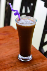 Iced coffee in a glass with a purple straw on a wooden table