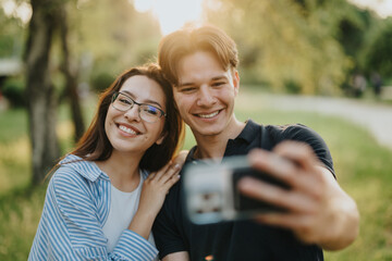 Smiling couple taking a selfie outside during a sunny day surrounded by greenery, radiating happiness, love, and connection in a lovely natural environment.