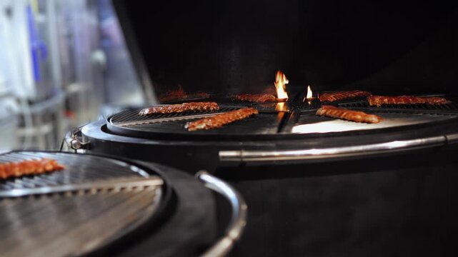 Grilling BBQ ribs rotate on over open flame on barbecue grill with intense heat and smoke.