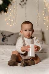 Little boy sitting on bed in knitted clothes and holding a candle