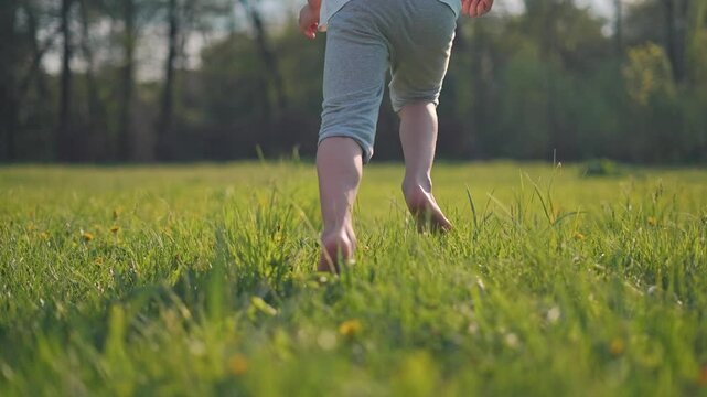 Child in motion runs quickly through vibrant nature field under bright sky. Barefoot legs move fast across summer grass. Child motion fills green field. Nature flows with every barefoot step of child.