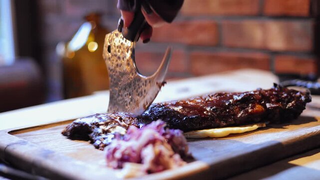 Slicing barbecued ribs with rustic cleaver on wooden board in restaurant.