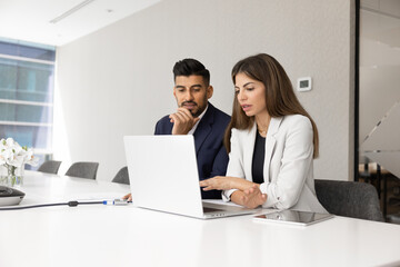 Diverse couple of serious managers talking at laptop