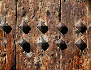 old grained and textured wooden door or gate detail. cracks and decorative rusty spikes with square...
