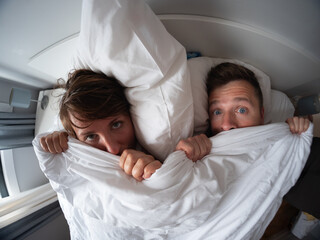 Middle aged couple lying under the blanket looking surprised. problems in life