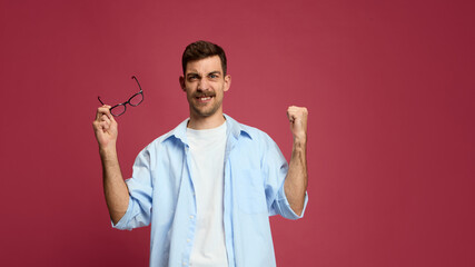 Excited man holding glasses and raising fist showing joy and satisfaction. Concept of success, achievement celebration, influencer content, social media reaction, and motivation in marketing.