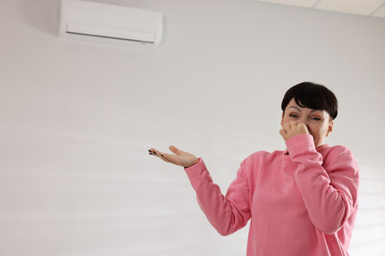 Woman feeling bad smell from air conditioner indoors, space for text
